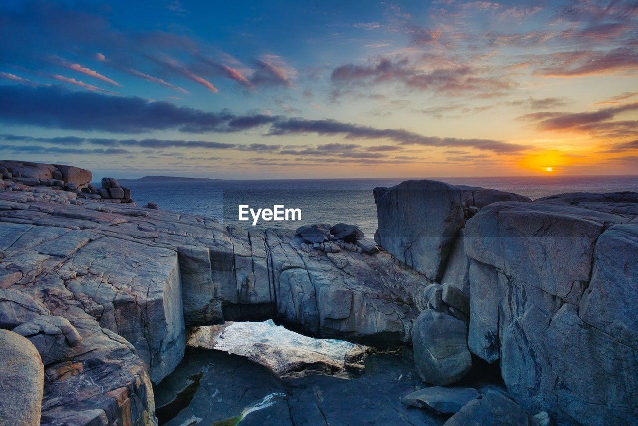 rocks on beach against sky during sunset