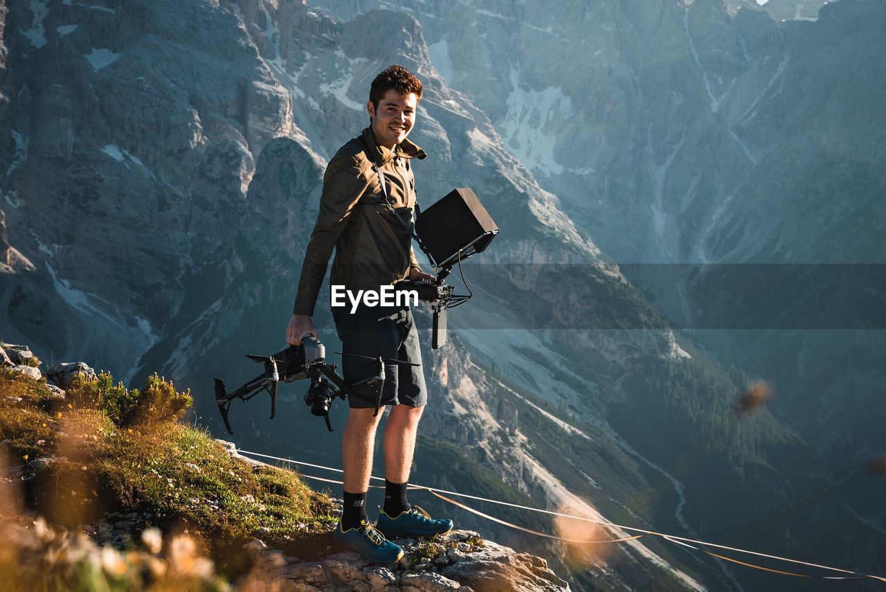 Portrait of young man standing holding drone while standing on mountain