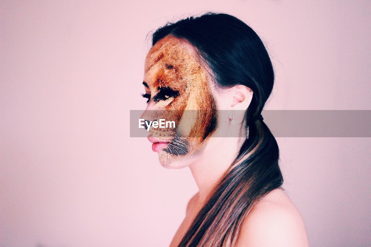 Close-up of young woman with face paint over pink background