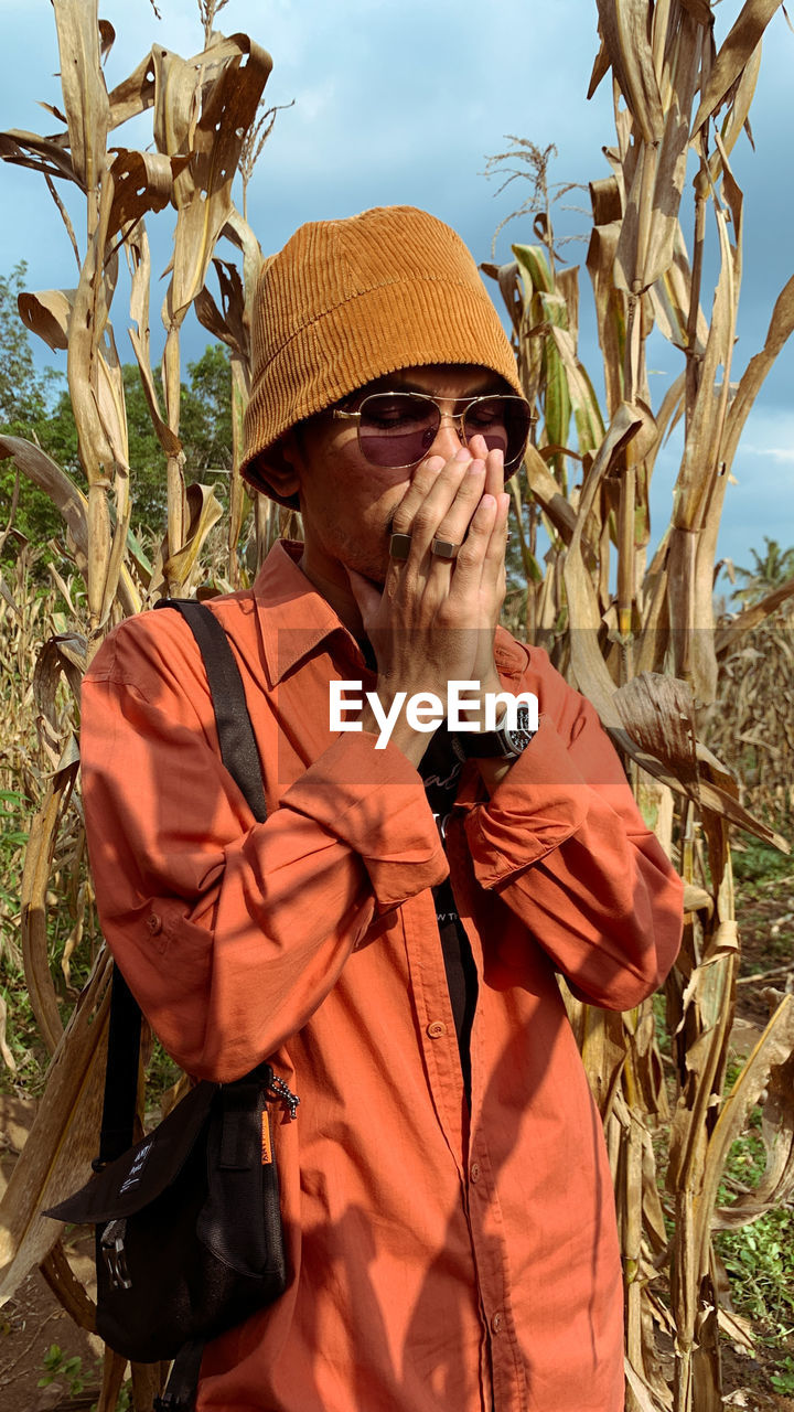 Side view of man wearing hat standing amidst plants on field