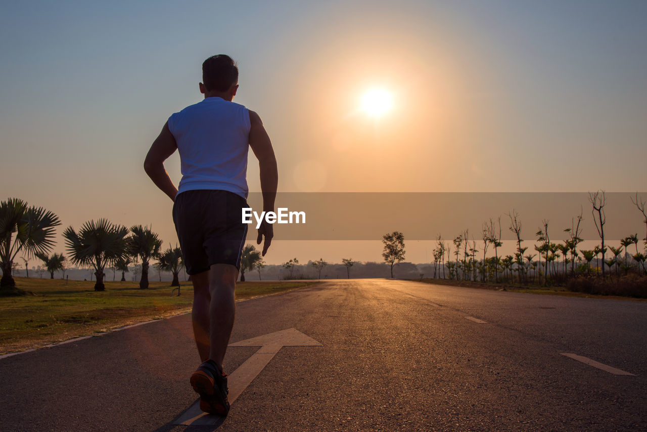 FULL LENGTH REAR VIEW OF MAN RUNNING ON ROAD AGAINST SKY