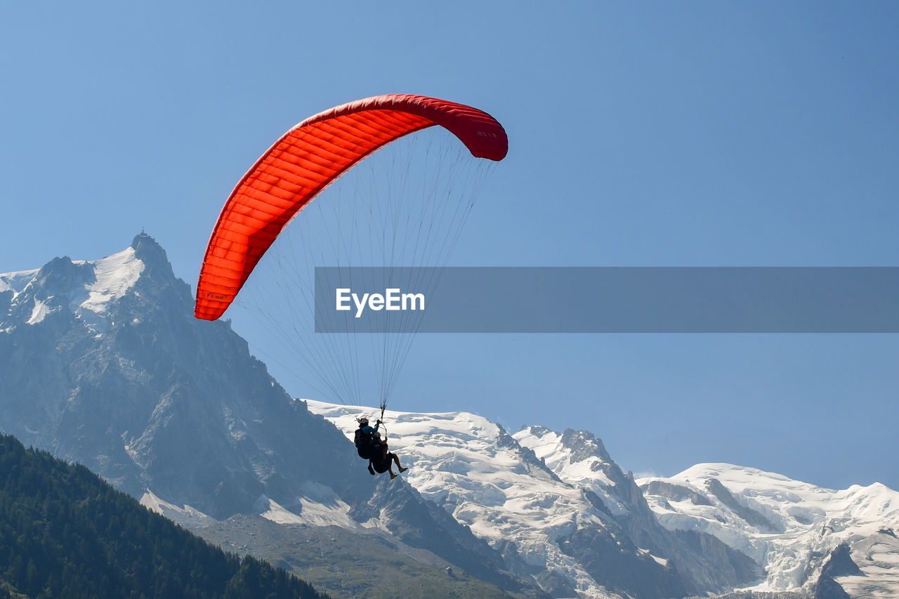 Red paraglider flying in front of the mont blanc mountain range in the french alps, chamonix, france