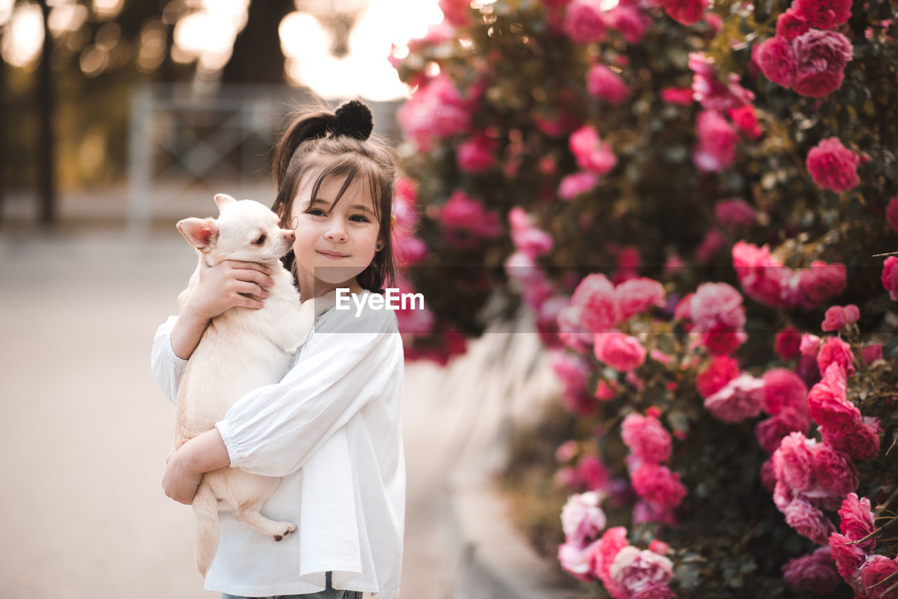 Smiling baby girl holding pet dog over nature background close up. looking at camera.