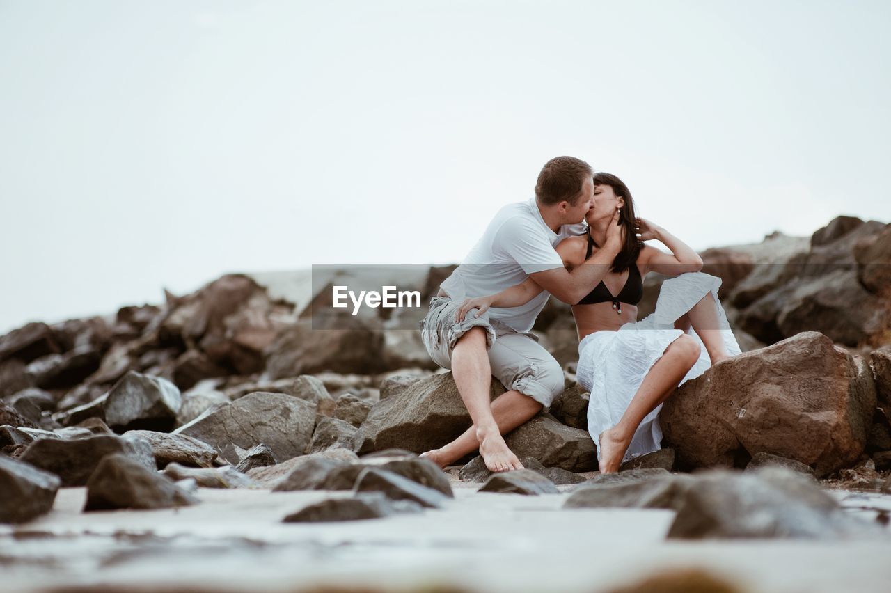 Couple kissing at beach against sky