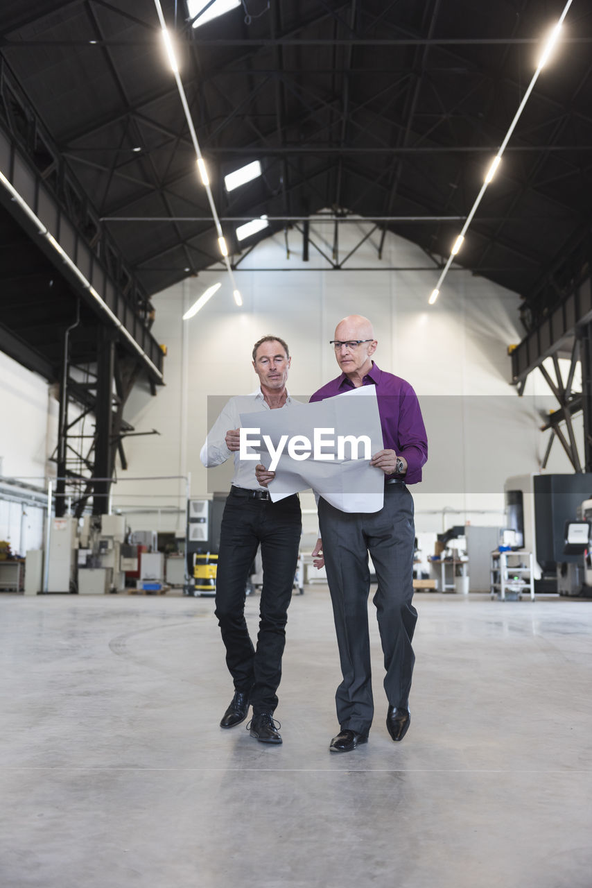 Two businessmen with plan walking in factory shop floor