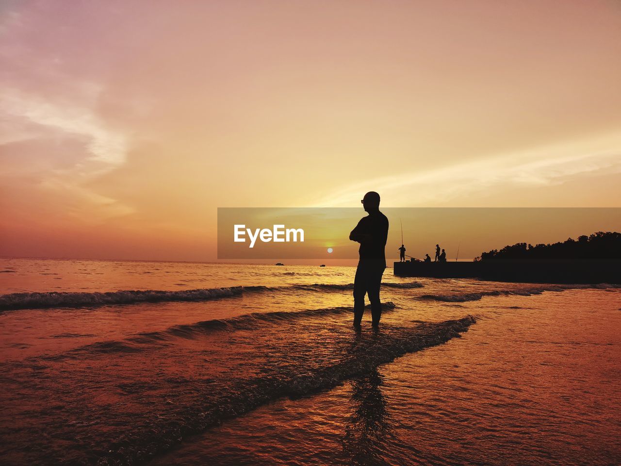 Silhouette man standing on shore at beach against sky during sunset