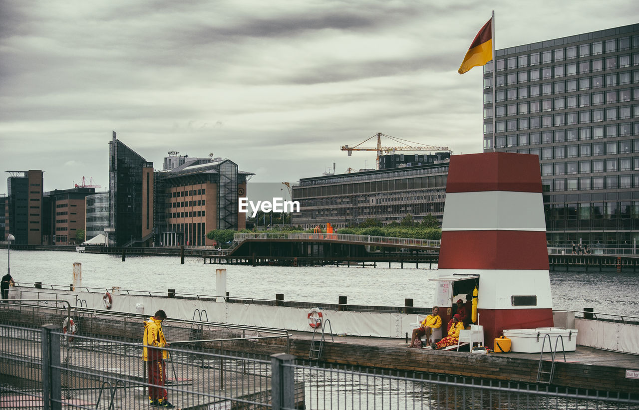 PEOPLE ON RIVER BY BUILDINGS AGAINST SKY