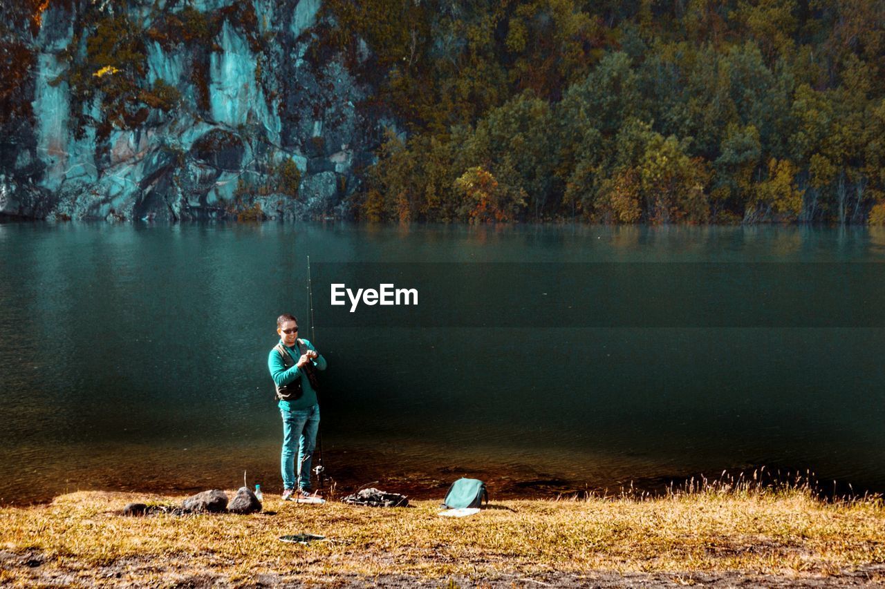 FULL LENGTH OF MAN STANDING BY LAKE DURING AUTUMN