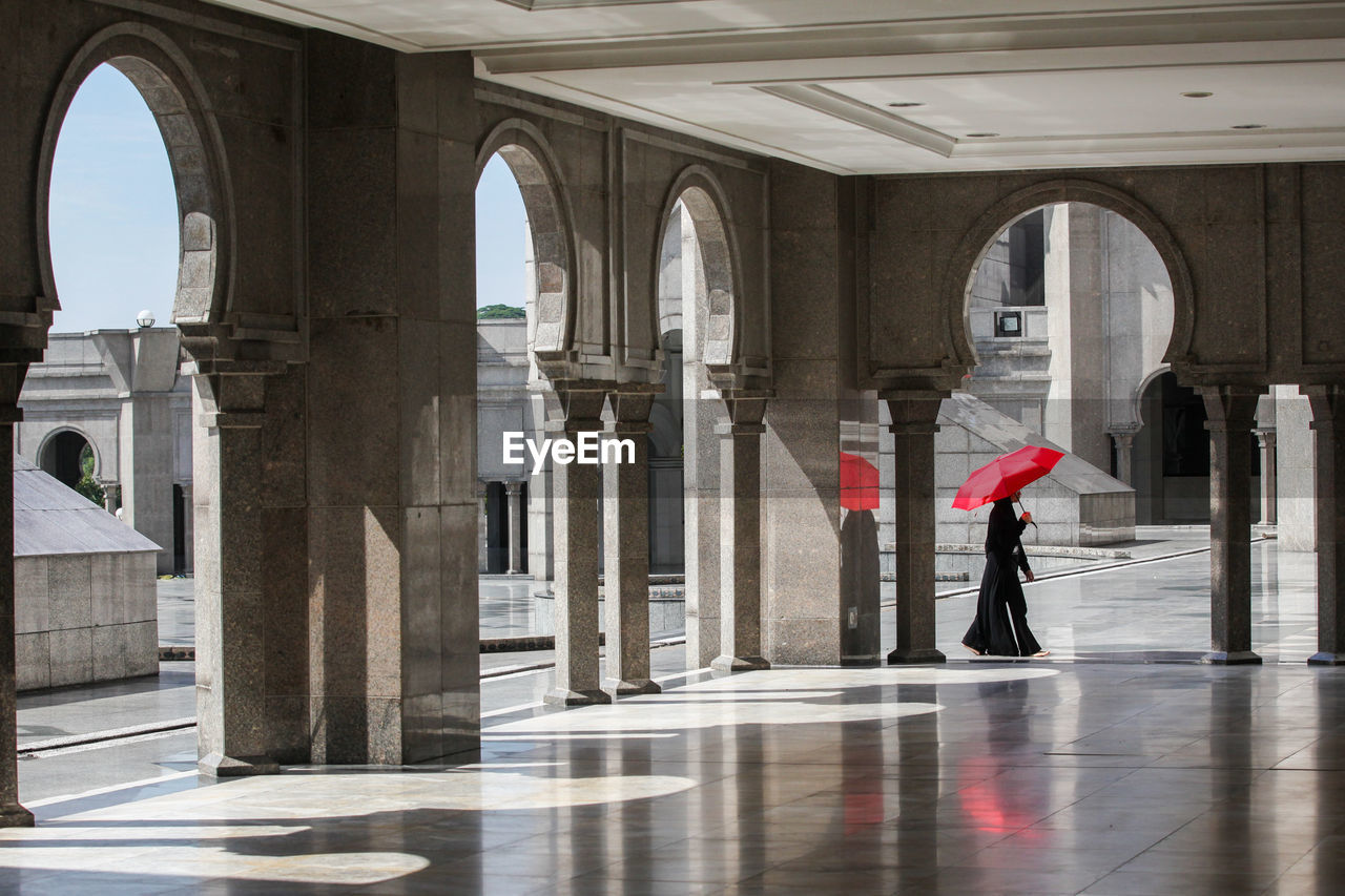 Side view of woman with umbrella walking against building