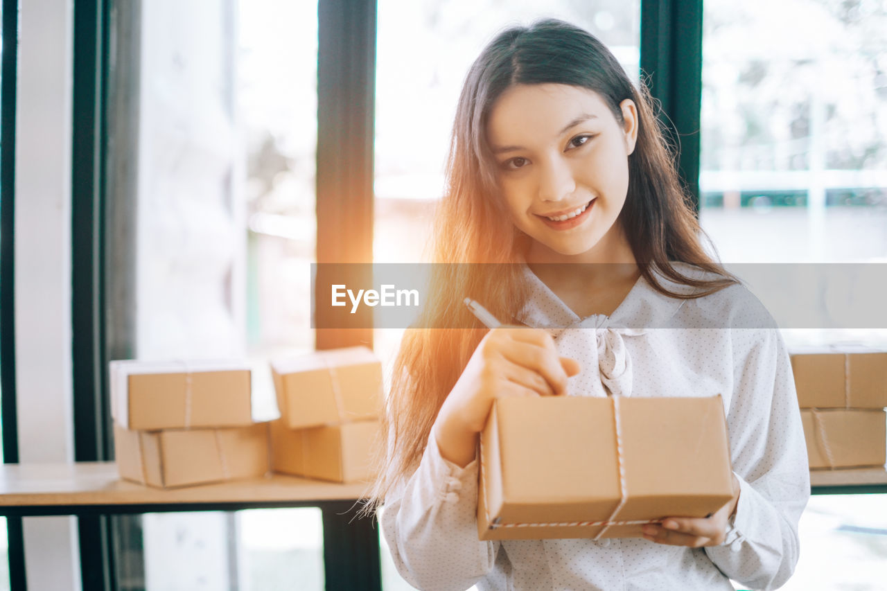 Portrait of young businesswoman writing on package at office