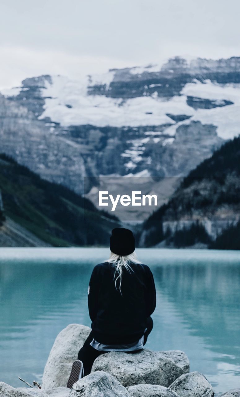 Rear view of woman sitting by lake against mountains