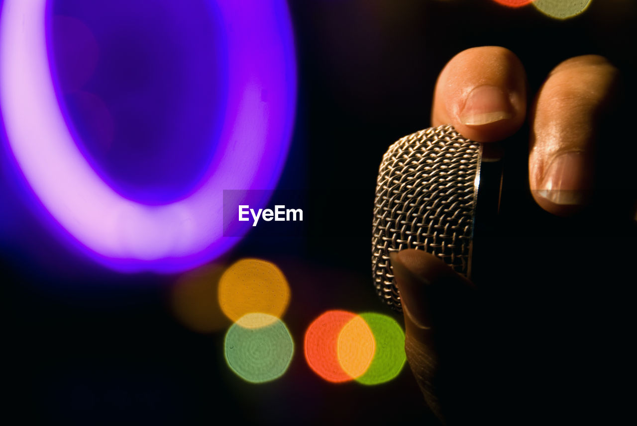 Cropped hand holding microphone against illuminated lights