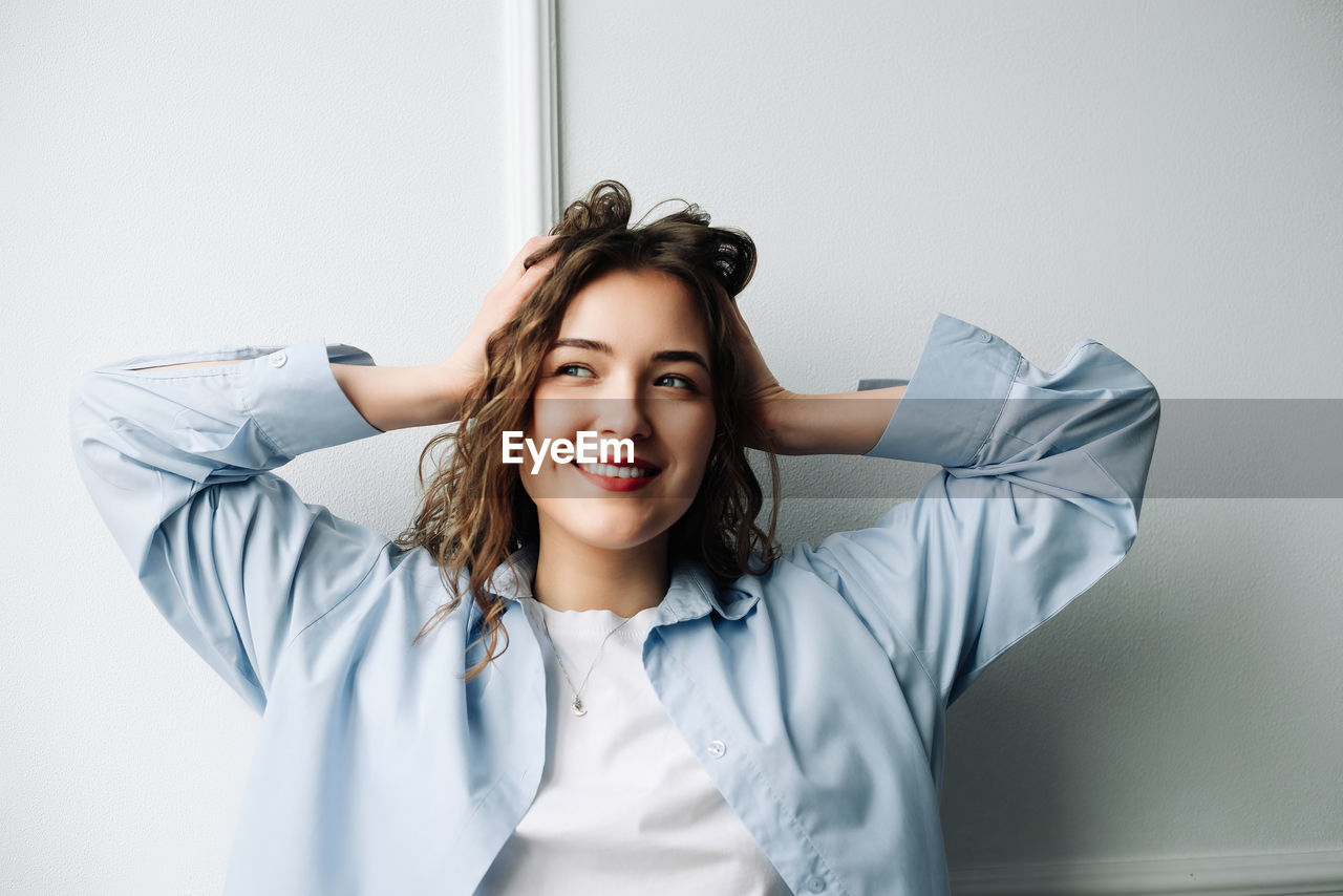 portrait of smiling young woman standing against wall