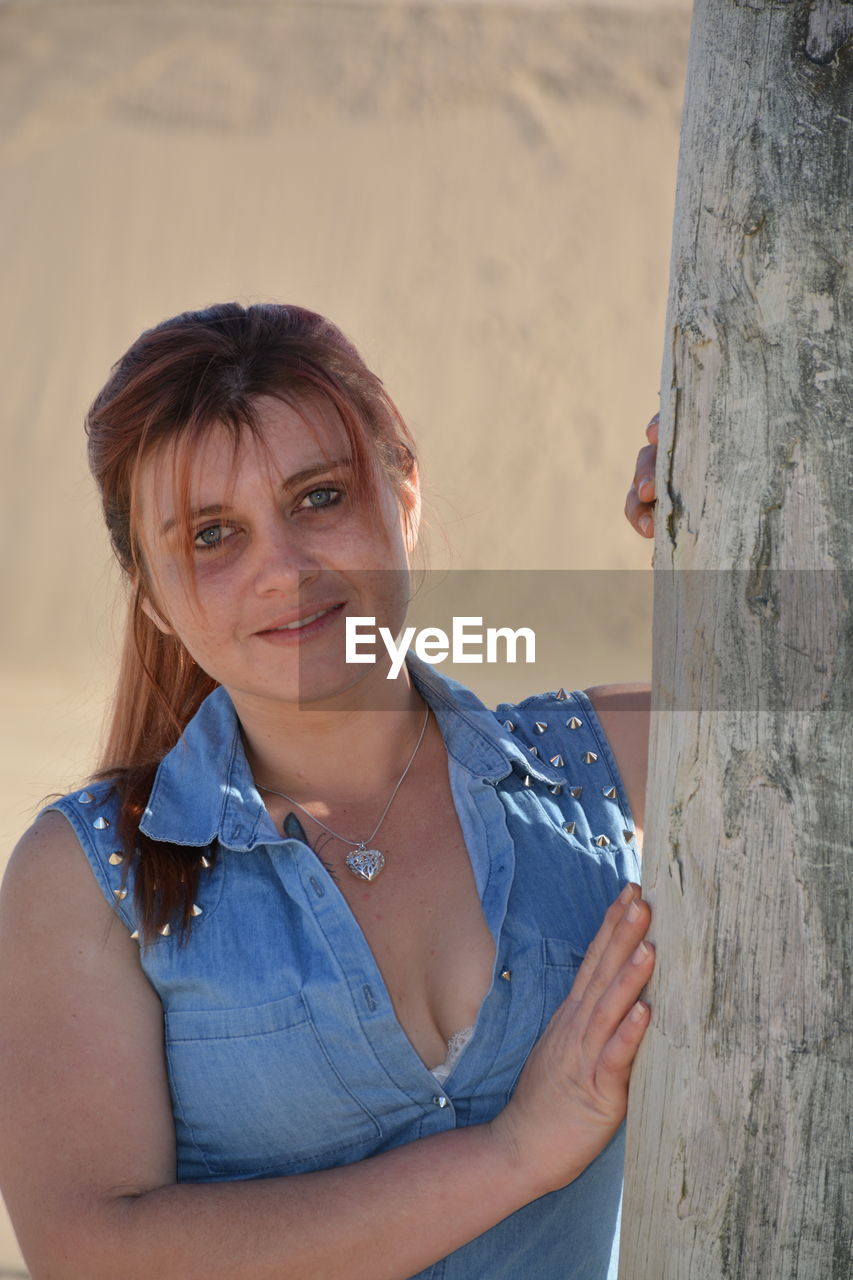 Portrait of young woman standing by tree trunk