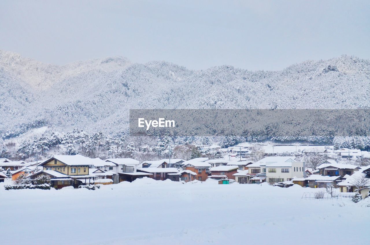 Houses on snow covered field by mountains against sky