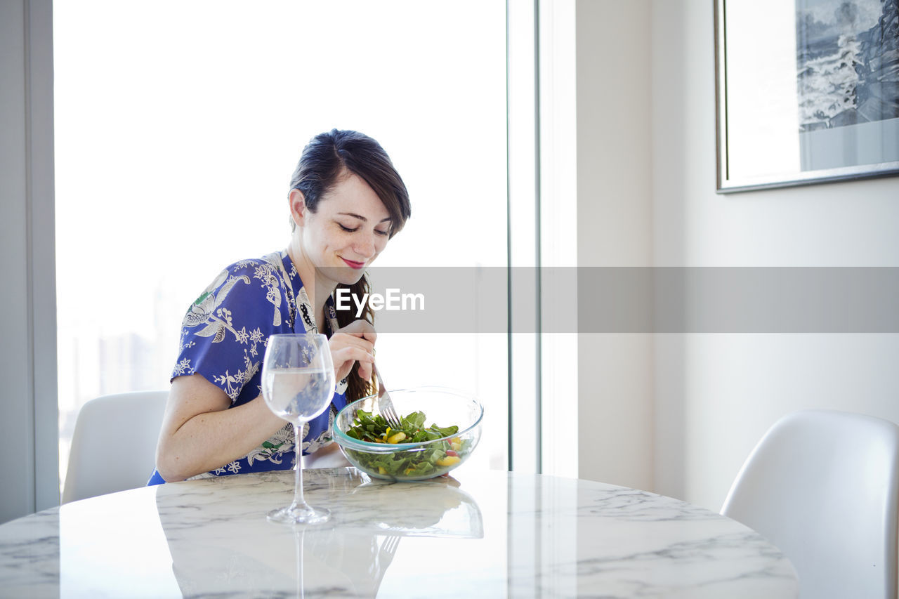 Woman eating salad while sitting by table home