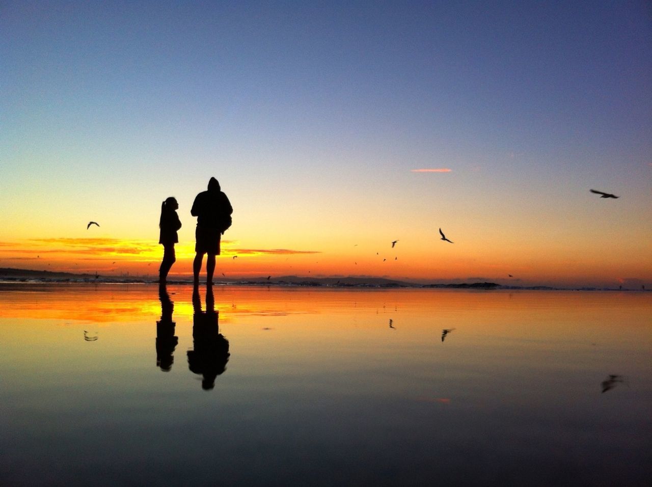 Two silhouette standing people on beach