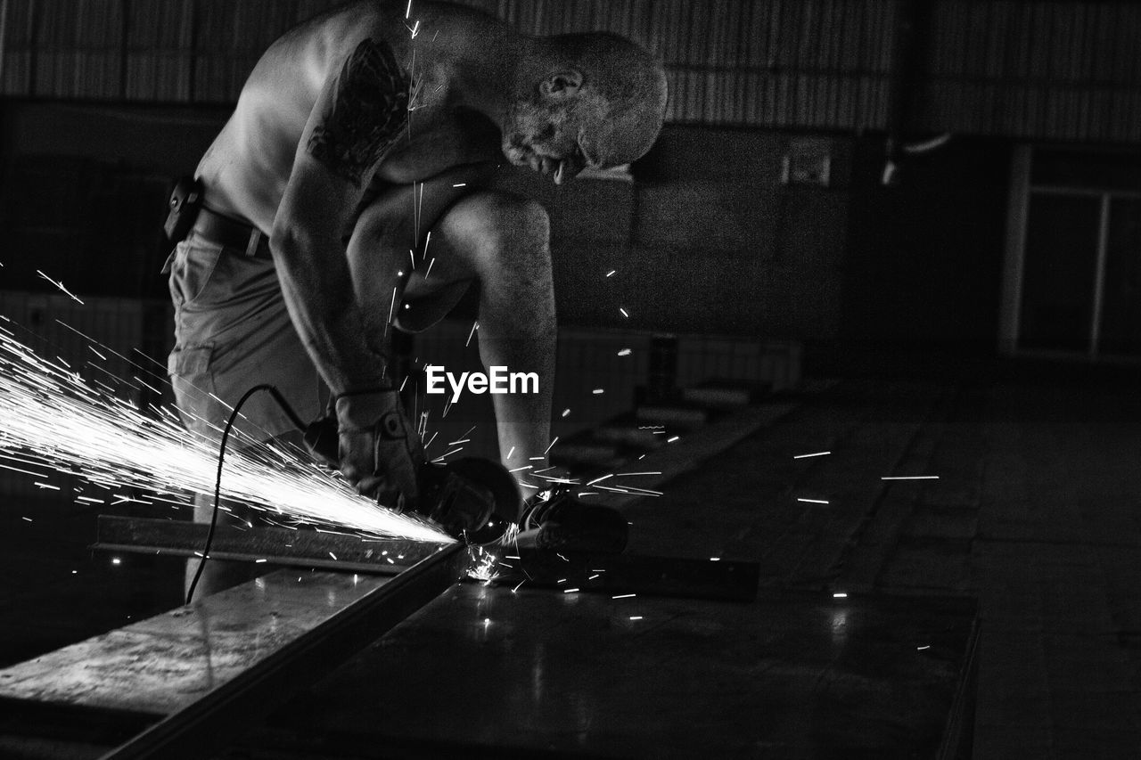 Side view of mature worker cutting metal in factory