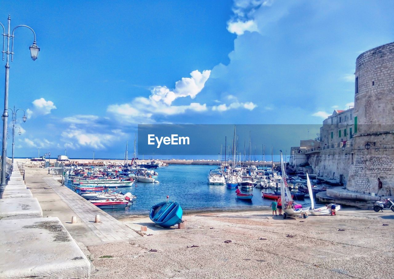 Sailboats moored at harbor against blue sky