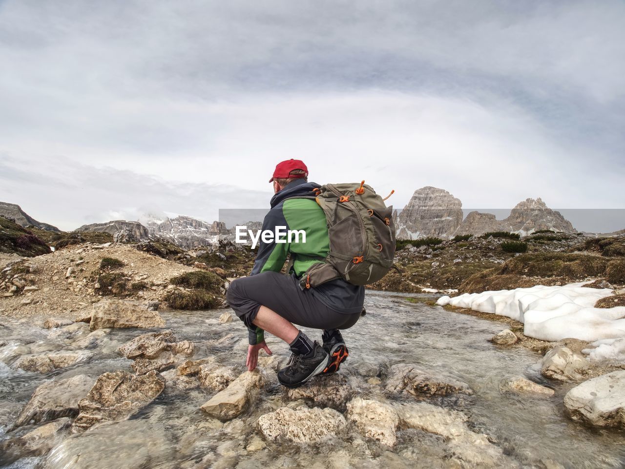 Hiker man with backpack crossing stream on stones in dolomiti mountains. hiking and leisure theme