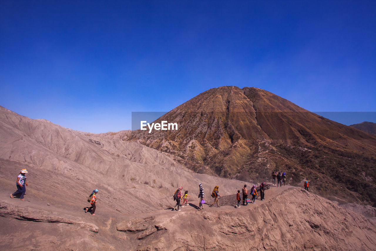 People on desert against clear blue sky