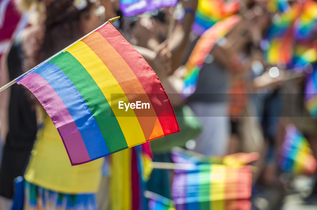 Close-up of rainbow flag with crowd in background during parade