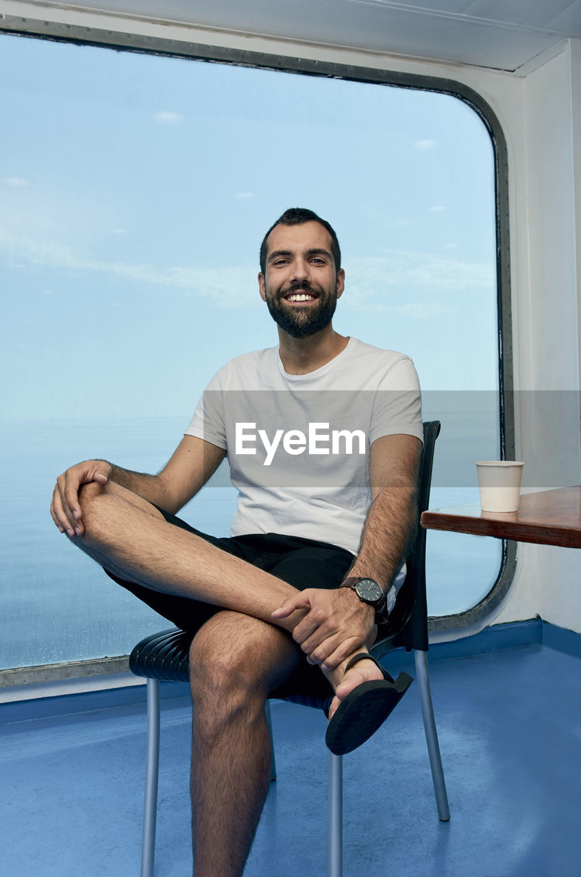 Portrait of smiling young man sitting on chair in cruise ship