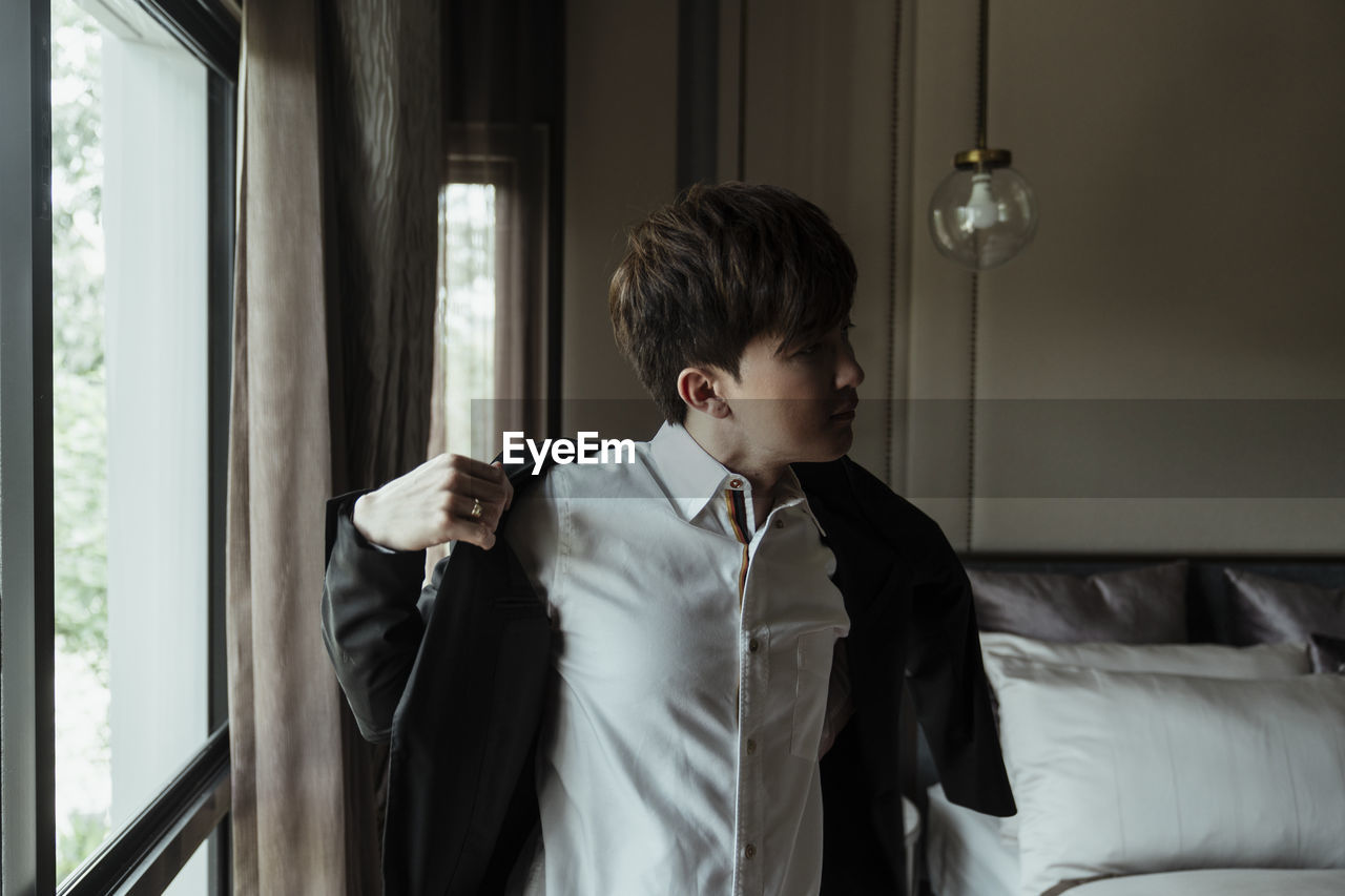 Young man looking through window at home