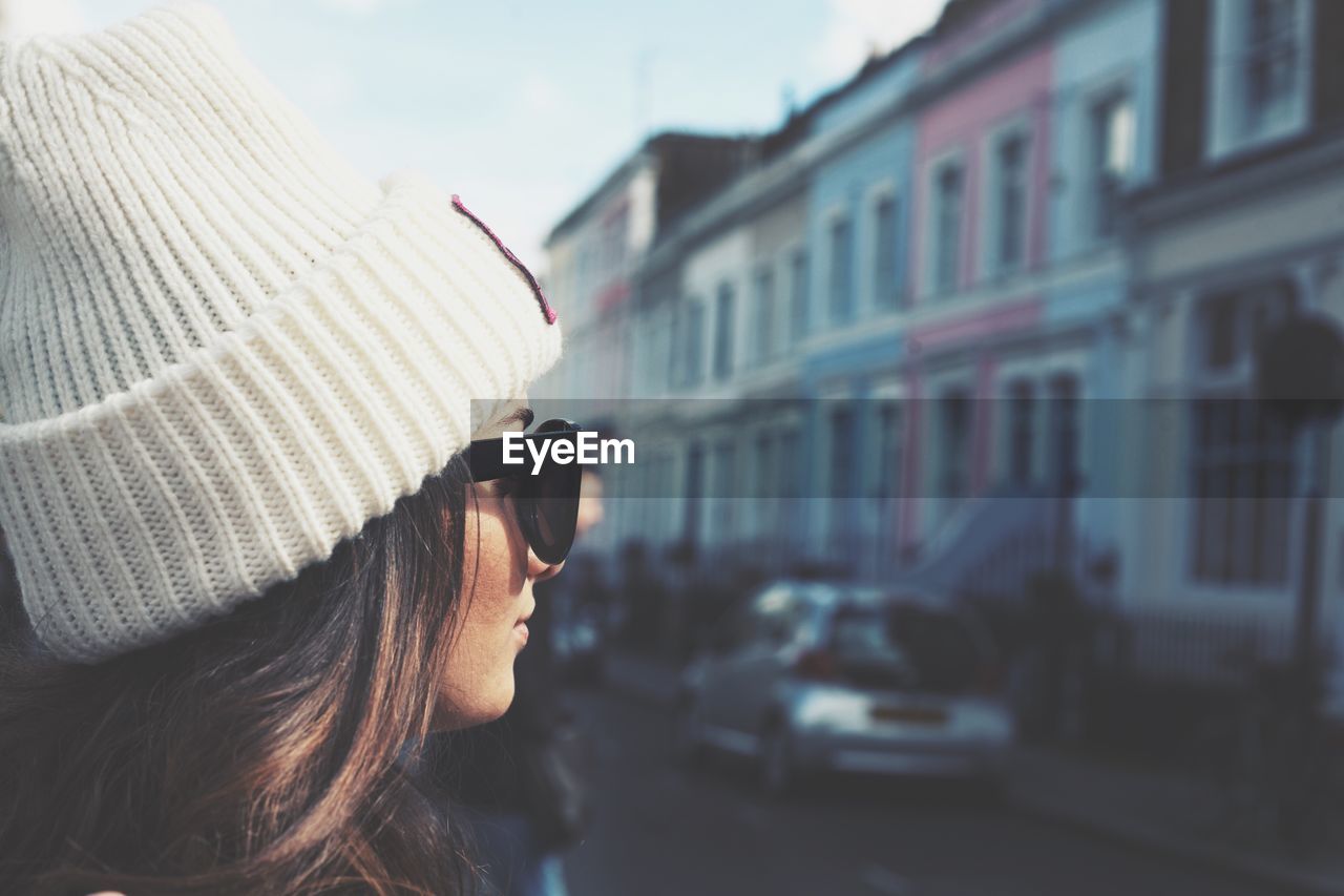 Close-up of woman wearing sunglasses and knit hat while looking away in city