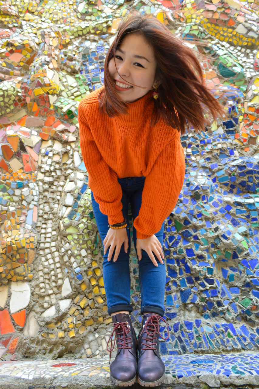 Portrait of smiling young woman bending against mosaic