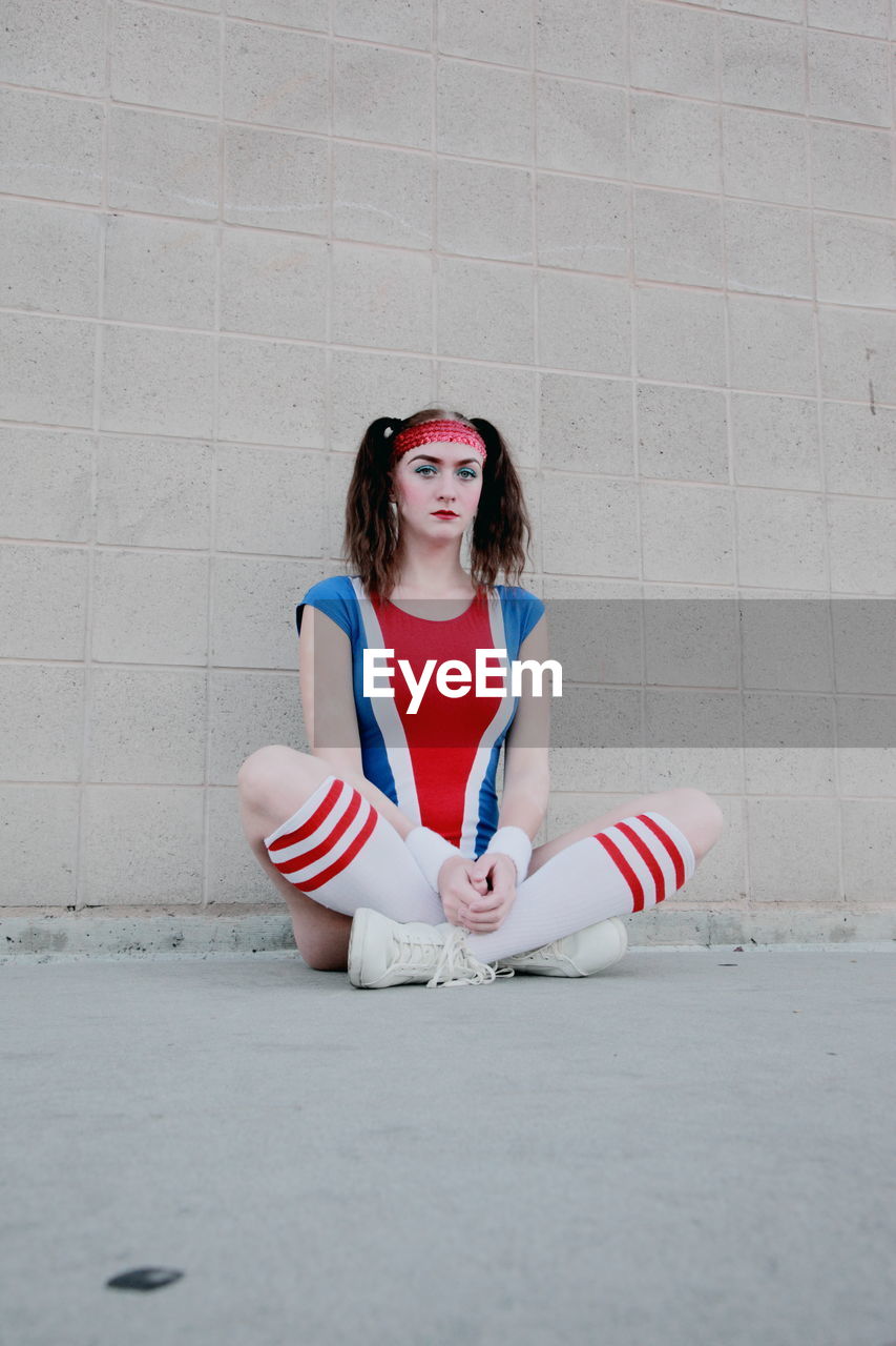 Portrait of cheerleader sitting on footpath against wall