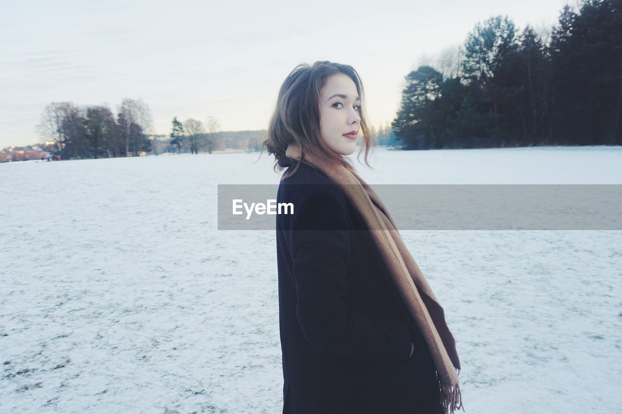 Portrait of beautiful woman standing on snow covered landscape against sky