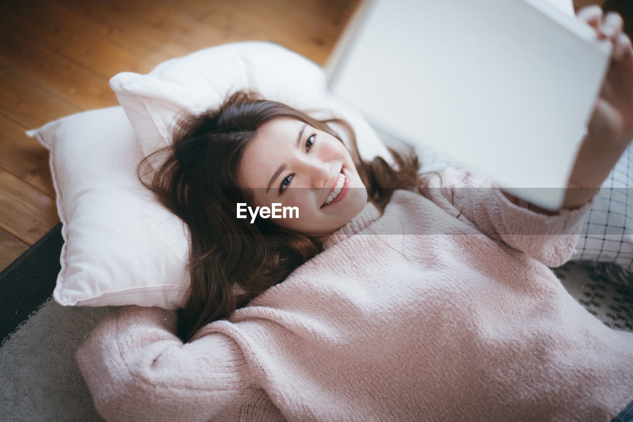 Smiling woman reading book on bed at home