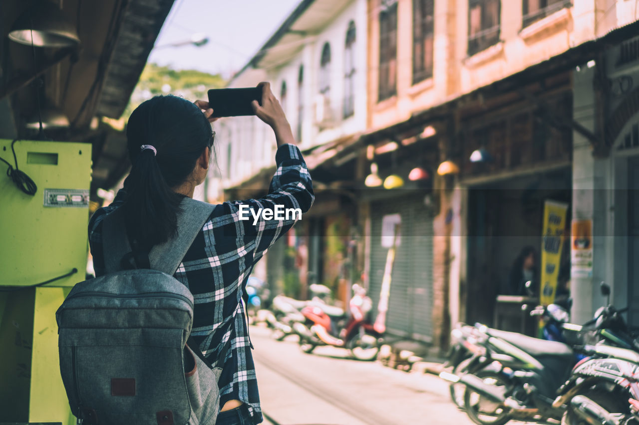 REAR VIEW OF MAN PHOTOGRAPHING ON STREET