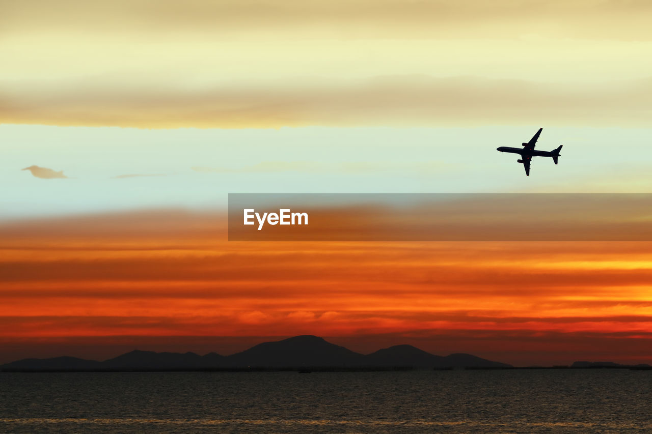 Silhouette airplane flying in sky during sunset