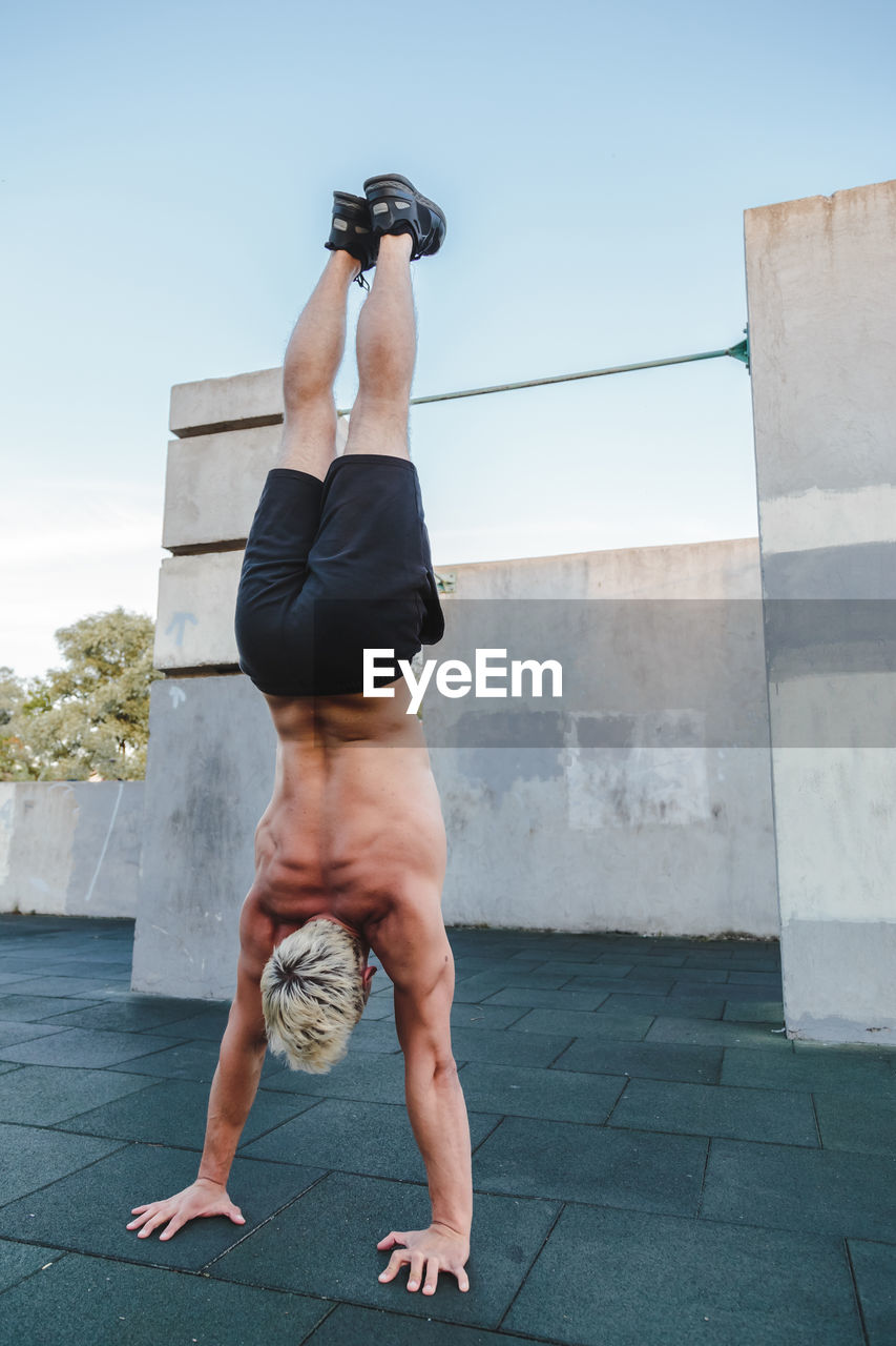 Full length of shirtless man exercising against sky