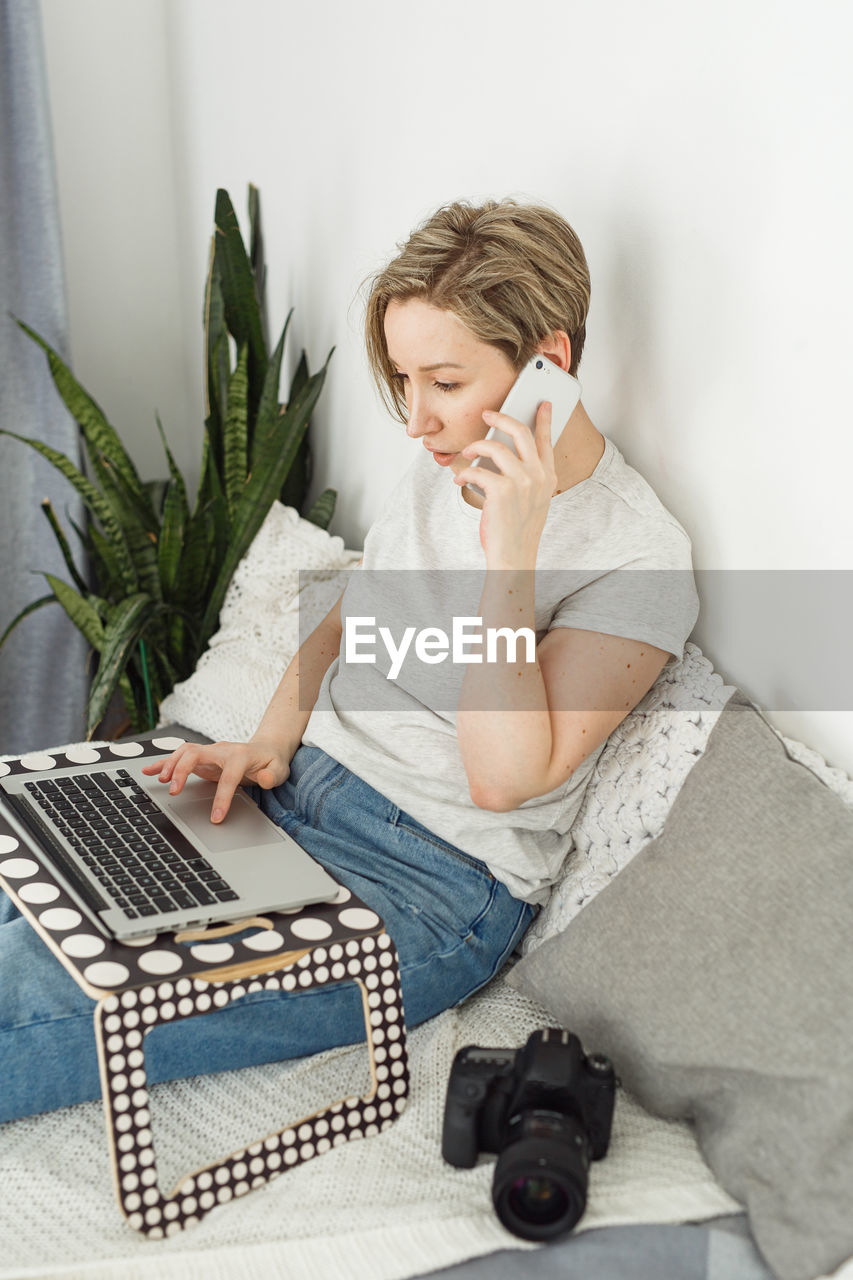 Young woman using mobile phone while sitting on bed at home