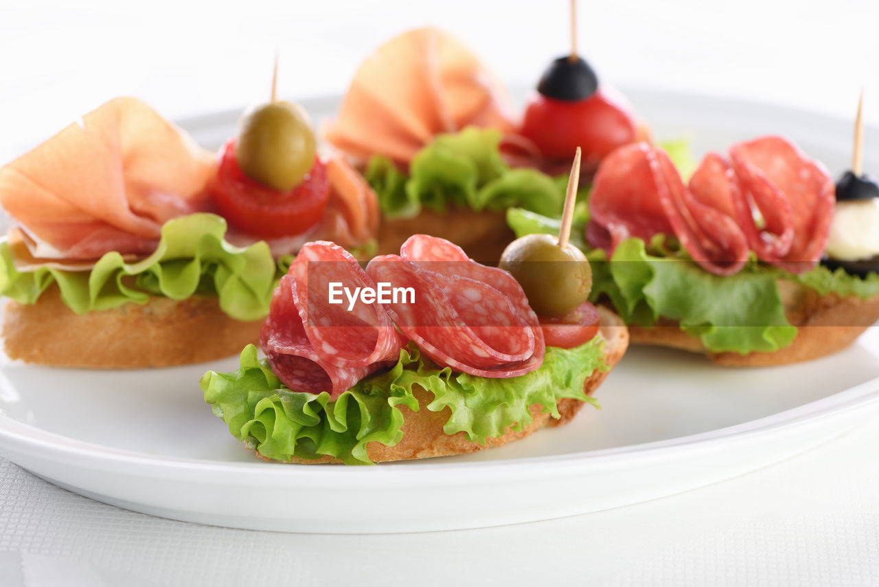 Tender baguette canapes with lettuce, salami or ham, tomatoes, mozzarella and olive