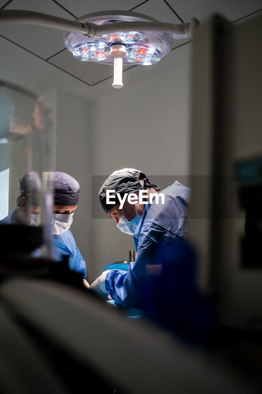 Veterinarian surgeons and nurses in uniform concentrating and operating dog using special equipment in operating room of contemporary hospital