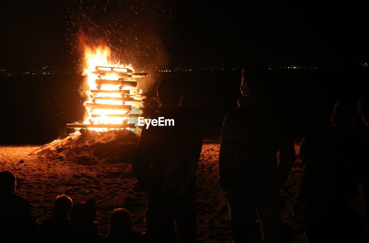 Silhouette of young people by bonfire on the beach 