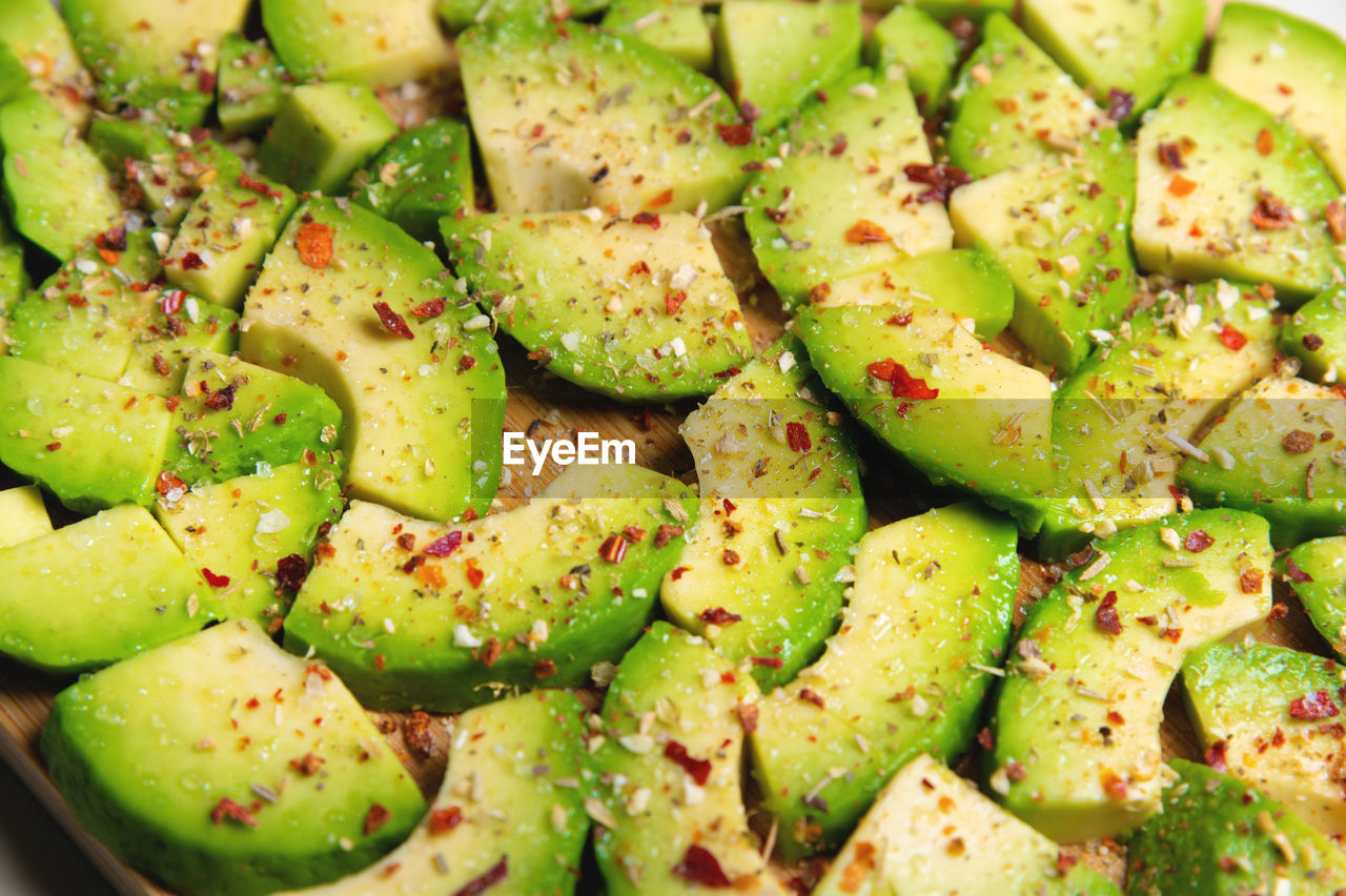 Large slices of sliced ripe avocado lie textured on a wooden cutting board. sprinkled with spices