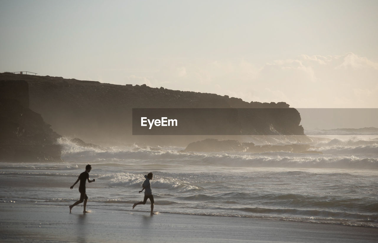 MEN ON BEACH AGAINST SKY