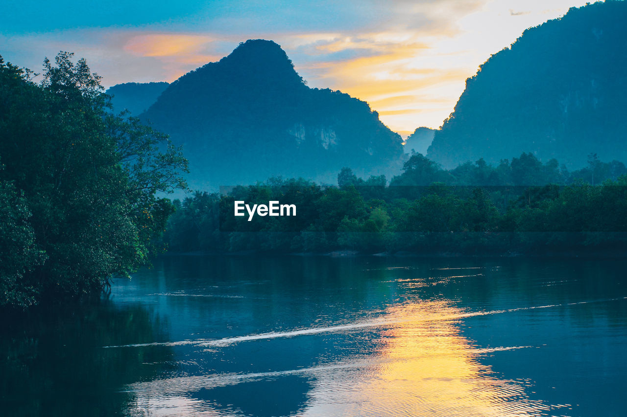 Scenic view of lake by trees against sky during sunset