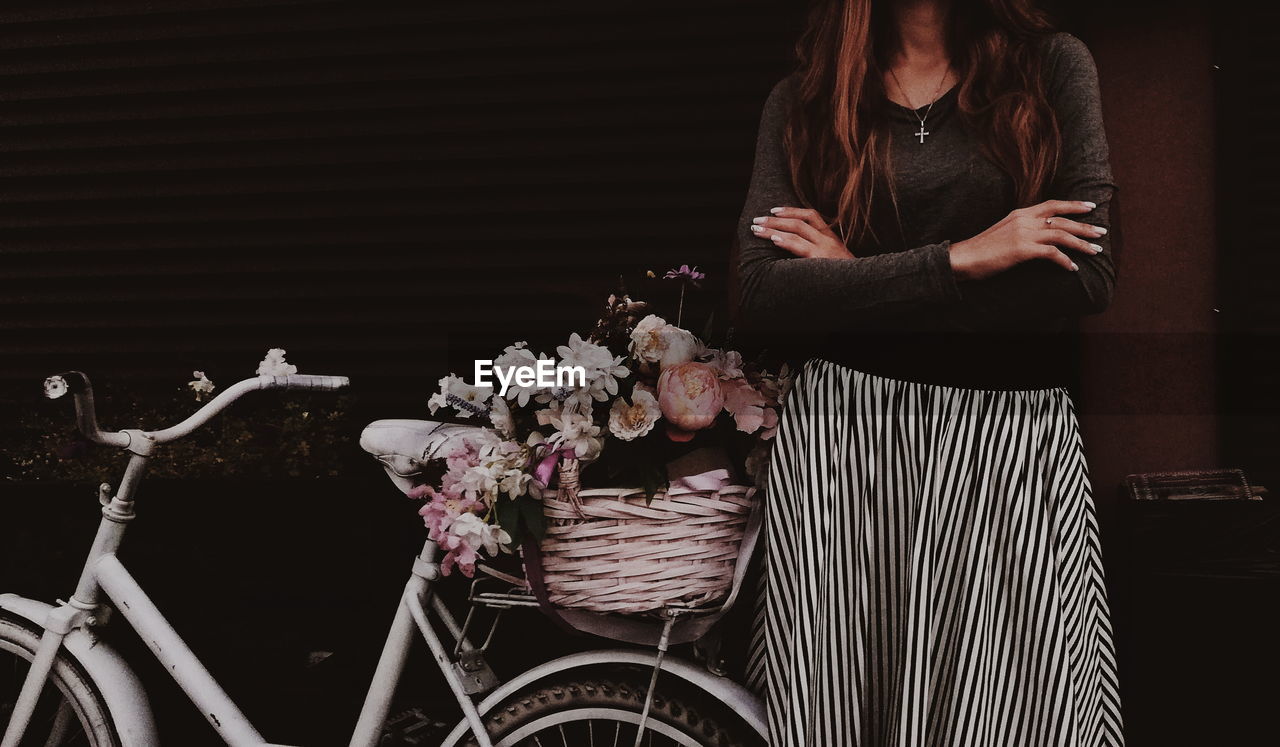 Midsection of woman standing by bicycle and flowers in city