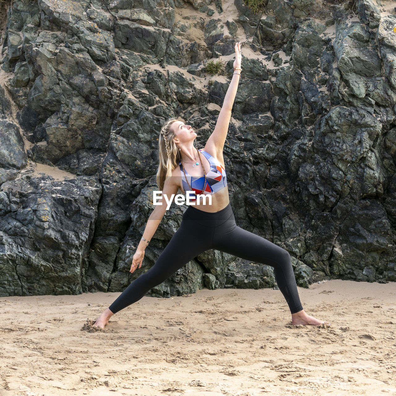 Full length of young woman practicing yoga at beach against rock formation