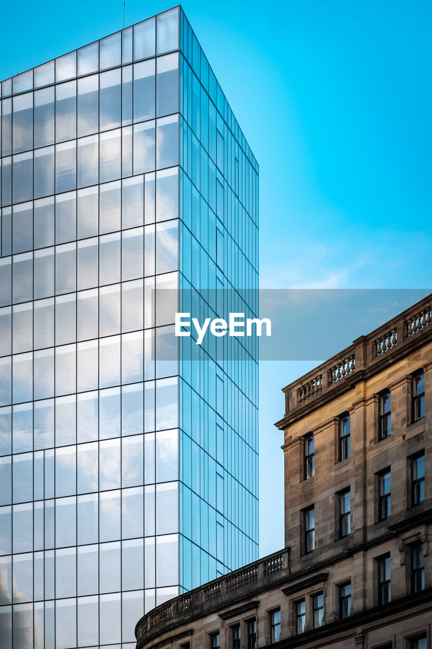 Low angle view of modern and old buildings against blue sky