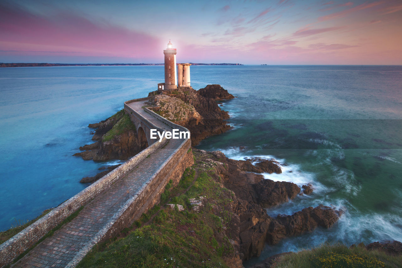 Lighthouse by sea against sky during sunset