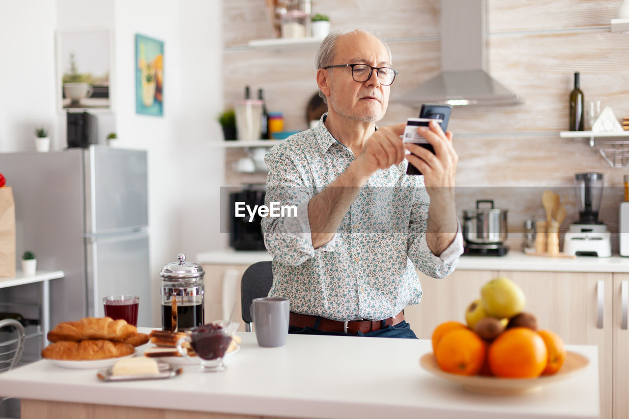 Senior man holding credit card while using laptop at home