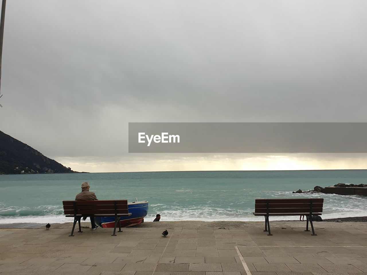 PEOPLE SITTING ON BENCH AT BEACH AGAINST SKY