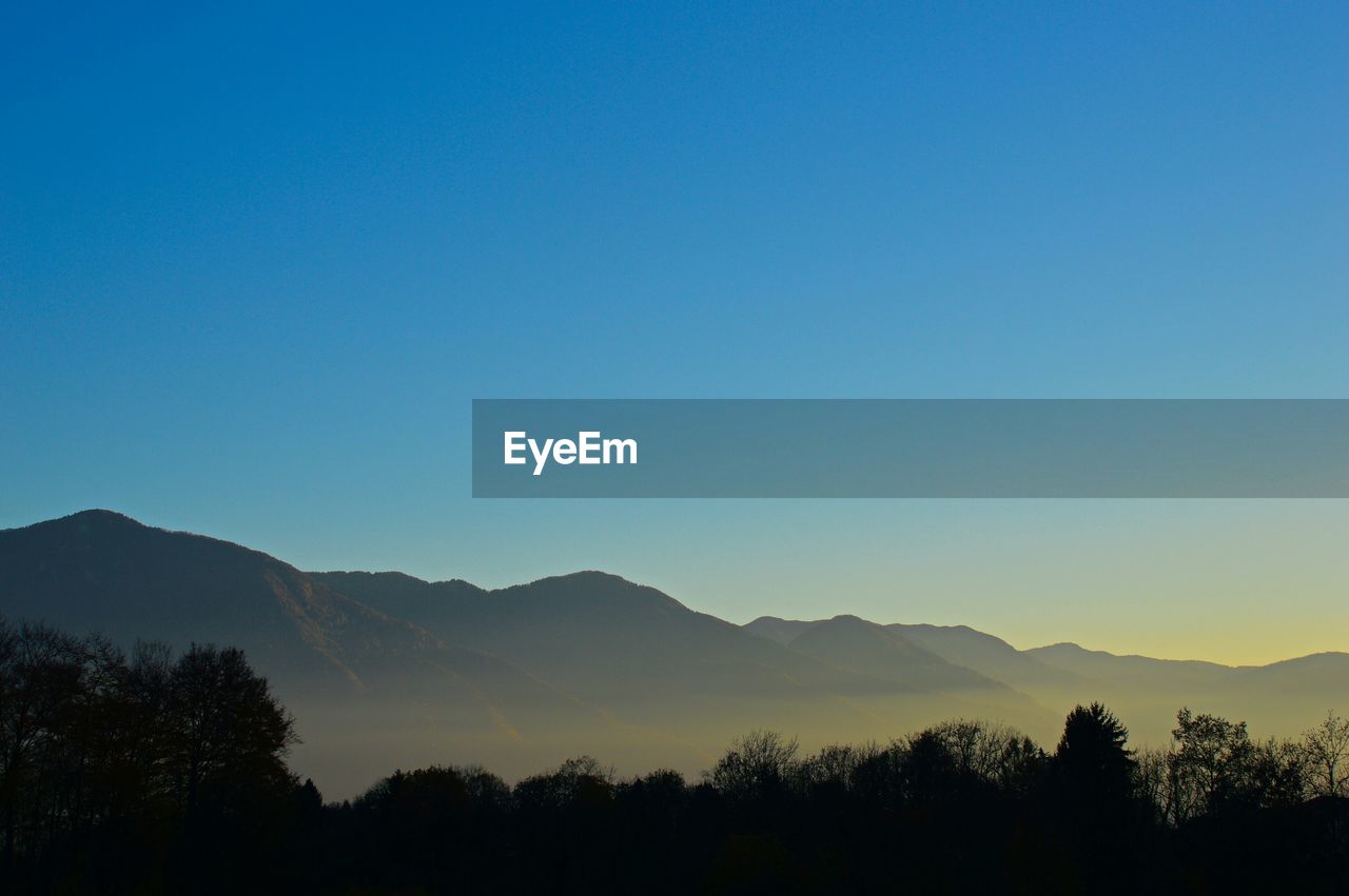 Silhouette trees against mountains at sunset